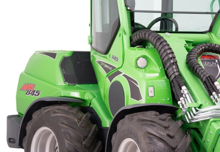 Close-up view of the Avant 845 GT mini loader, focusing on the hydraulic hoses and part of the enclosed cabin. The green loader showcases rugged tires and detailing, emphasizing its robust design for heavy-duty tasks.